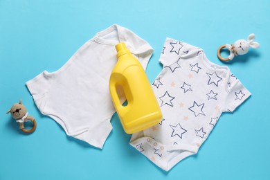 Photo of Bottle of fabric softener, toys and baby clothes on light blue background, flat lay