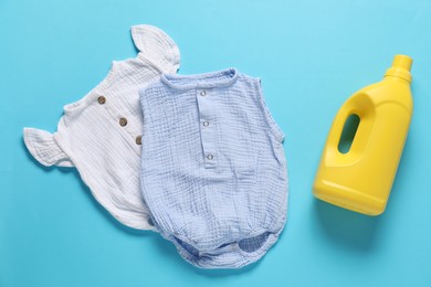 Photo of Bottle of fabric softener and baby clothes on light blue background, flat lay