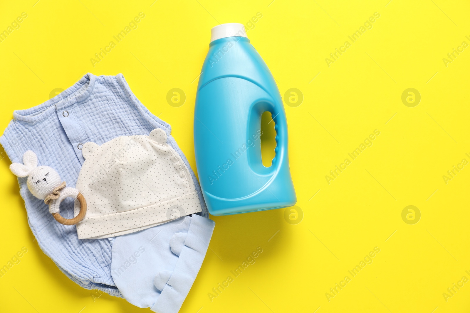Bottle of fabric softener, toy and baby clothes on yellow background, flat lay. Space for text Photo of Bottle of fabric softener, toy and baby clothes on yellow background, flat lay. Space for text