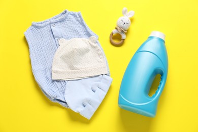 Photo of Bottle of fabric softener, toy and baby clothes on yellow background, flat lay