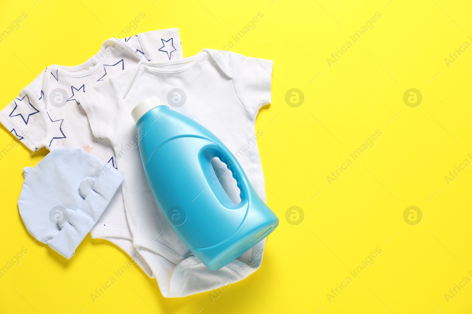 Bottle of fabric softener and baby clothes on yellow background, flat lay. Space for text Photo of Bottle of fabric softener and baby clothes on yellow background, flat lay. Space for text