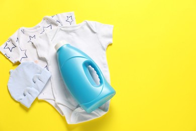 Photo of Bottle of fabric softener and baby clothes on yellow background, flat lay. Space for text