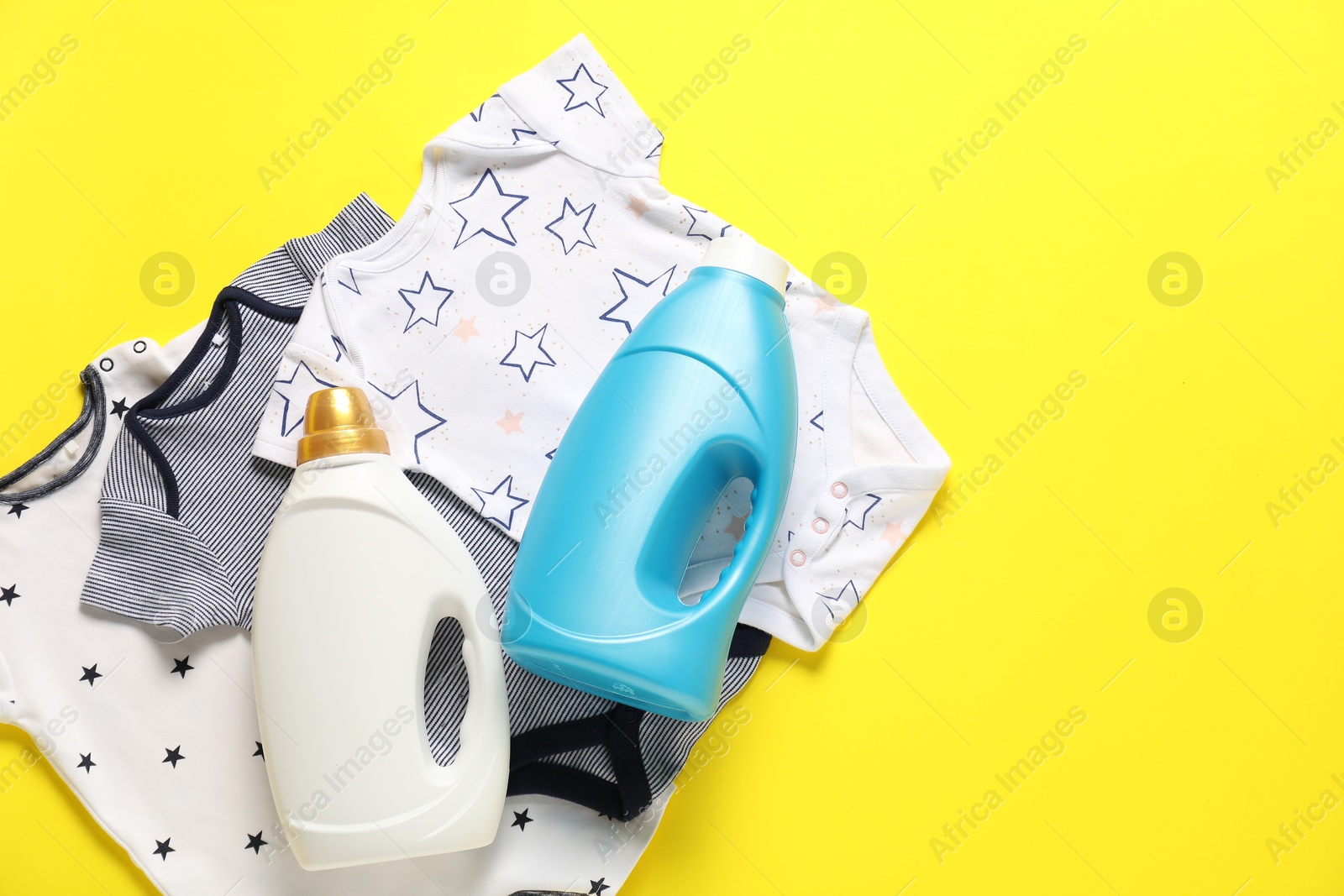 Bottles of fabric softener and baby clothes on yellow background, flat lay. Space for text Photo of Bottles of fabric softener and baby clothes on yellow background, flat lay. Space for text