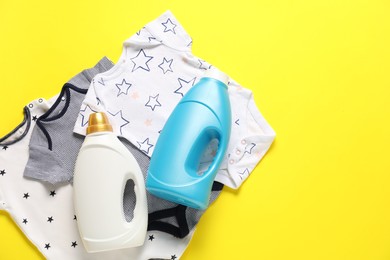 Photo of Bottles of fabric softener and baby clothes on yellow background, flat lay. Space for text