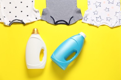 Photo of Bottles of fabric softener and baby clothes on yellow background, flat lay