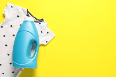 Photo of Bottle of fabric softener and baby clothes on yellow background, flat lay. Space for text