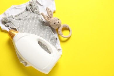 Photo of Bottle of fabric softener, toy and baby clothes on yellow background, flat lay. Space for text