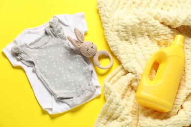 Photo of Bottle of fabric softener, toy, baby clothes and blanket on yellow background, closeup