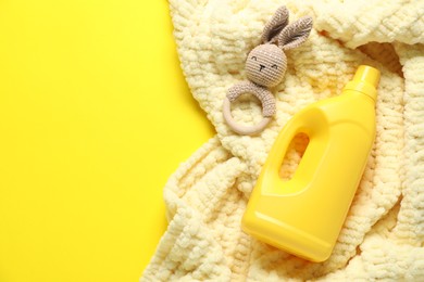 Photo of Bottle of fabric softener, toy and baby blanket on yellow background, flat lay. Space for text