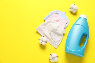 Photo of Bottle of fabric softener, cotton flowers and baby hats on yellow background, flat lay. Space for text