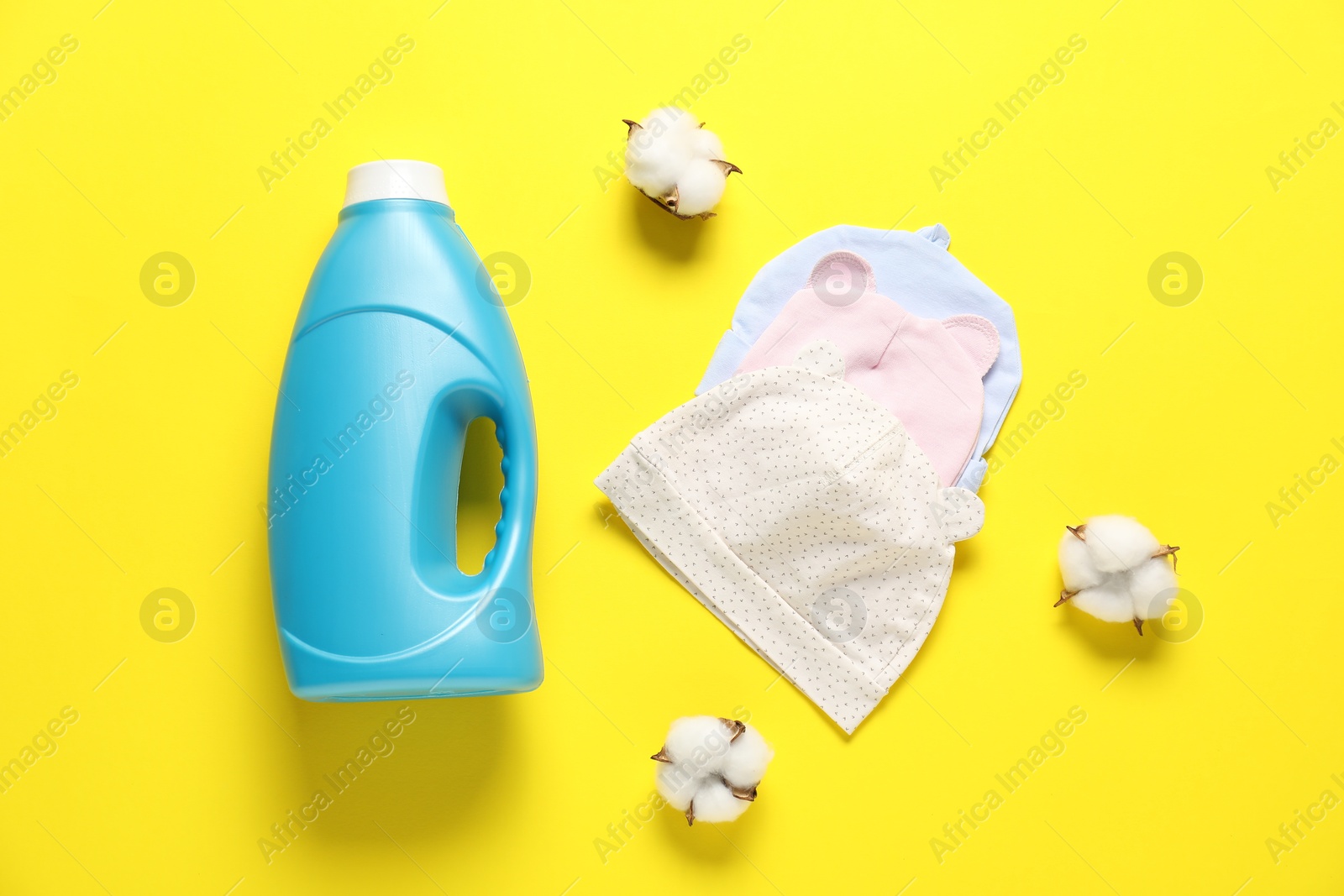 Bottle of fabric softener, cotton flowers and baby hats on yellow background, flat lay Photo of Bottle of fabric softener, cotton flowers and baby hats on yellow background, flat lay