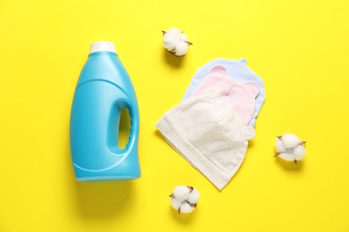 Photo of Bottle of fabric softener, cotton flowers and baby hats on yellow background, flat lay
