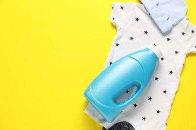 Photo of Bottle of fabric softener and baby clothes on yellow background, flat lay. Space for text