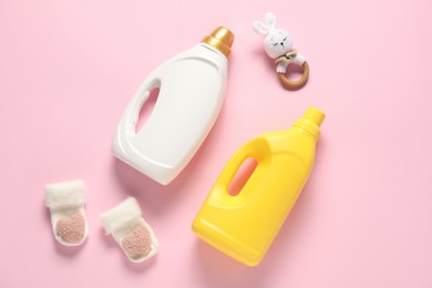 Photo of Bottles of fabric softener, toy and baby socks on pink background, flat lay