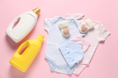 Photo of Bottles of fabric softener and baby clothes on pink background, flat lay