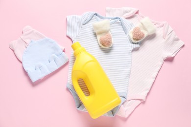 Photo of Bottle of fabric softener and baby clothes on pink background, flat lay