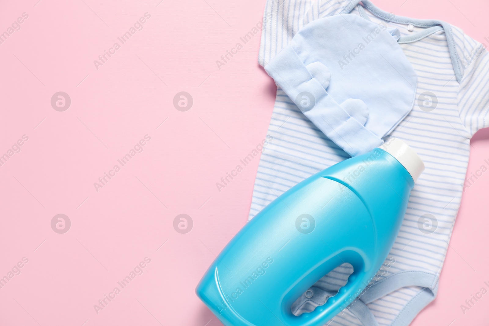 Bottle of fabric softener and baby clothes on pink background, flat lay. Space for text Photo of Bottle of fabric softener and baby clothes on pink background, flat lay. Space for text