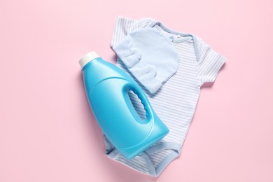 Photo of Bottle of fabric softener and baby clothes on pink background, flat lay