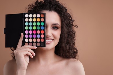Photo of Smiling woman covering eye with eyeshadow palette on beige background