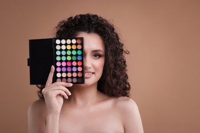 Photo of Smiling woman covering eye with eyeshadow palette on beige background