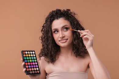 Photo of Smiling woman with eyeshadow palette and brush applying makeup on beige background