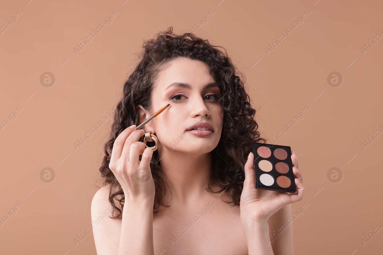Woman with eyeshadow palette and brush applying makeup on beige background Photo of Woman with eyeshadow palette and brush applying makeup on beige background