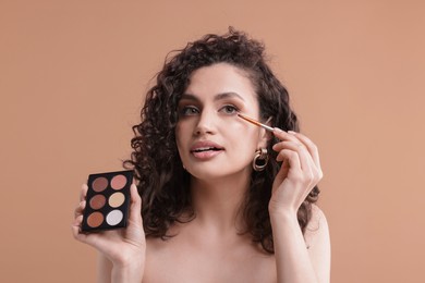 Photo of Woman with eyeshadow palette and brush applying makeup on beige background