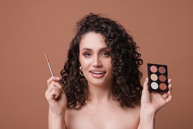 Photo of Smiling woman with eyeshadow palette and brush on brown background