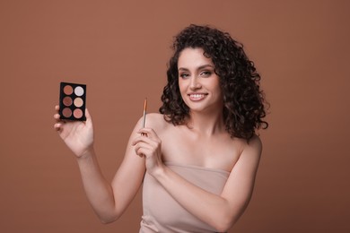 Photo of Smiling woman with eyeshadow palette and brush on brown background