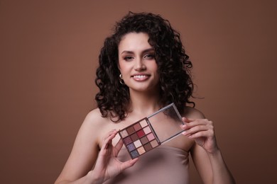 Photo of Smiling woman with eyeshadow palette on brown background