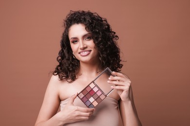 Photo of Smiling woman with eyeshadow palette on brown background