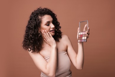 Photo of Surprised woman with eyeshadow palette on brown background