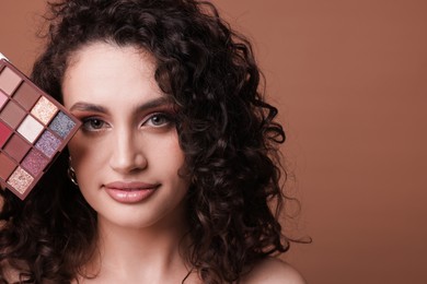 Photo of Woman with eyeshadow palette on brown background, closeup. Space for text