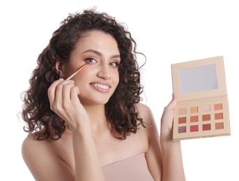 Photo of Smiling woman with eyeshadow palette and brush applying makeup on white background
