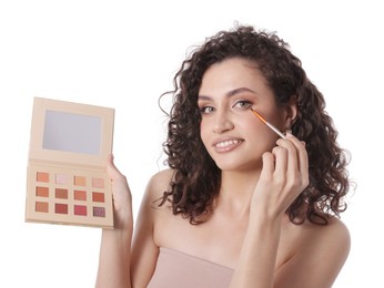 Photo of Smiling woman with eyeshadow palette and brush applying makeup on white background
