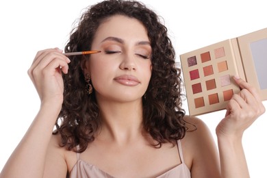Photo of Woman with eyeshadow palette and brush applying makeup on white background