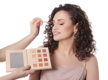 Photo of Makeup artist applying eyeshadows onto woman's face on white background, closeup
