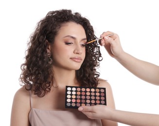 Photo of Makeup artist applying eyeshadows onto woman's face on white background, closeup