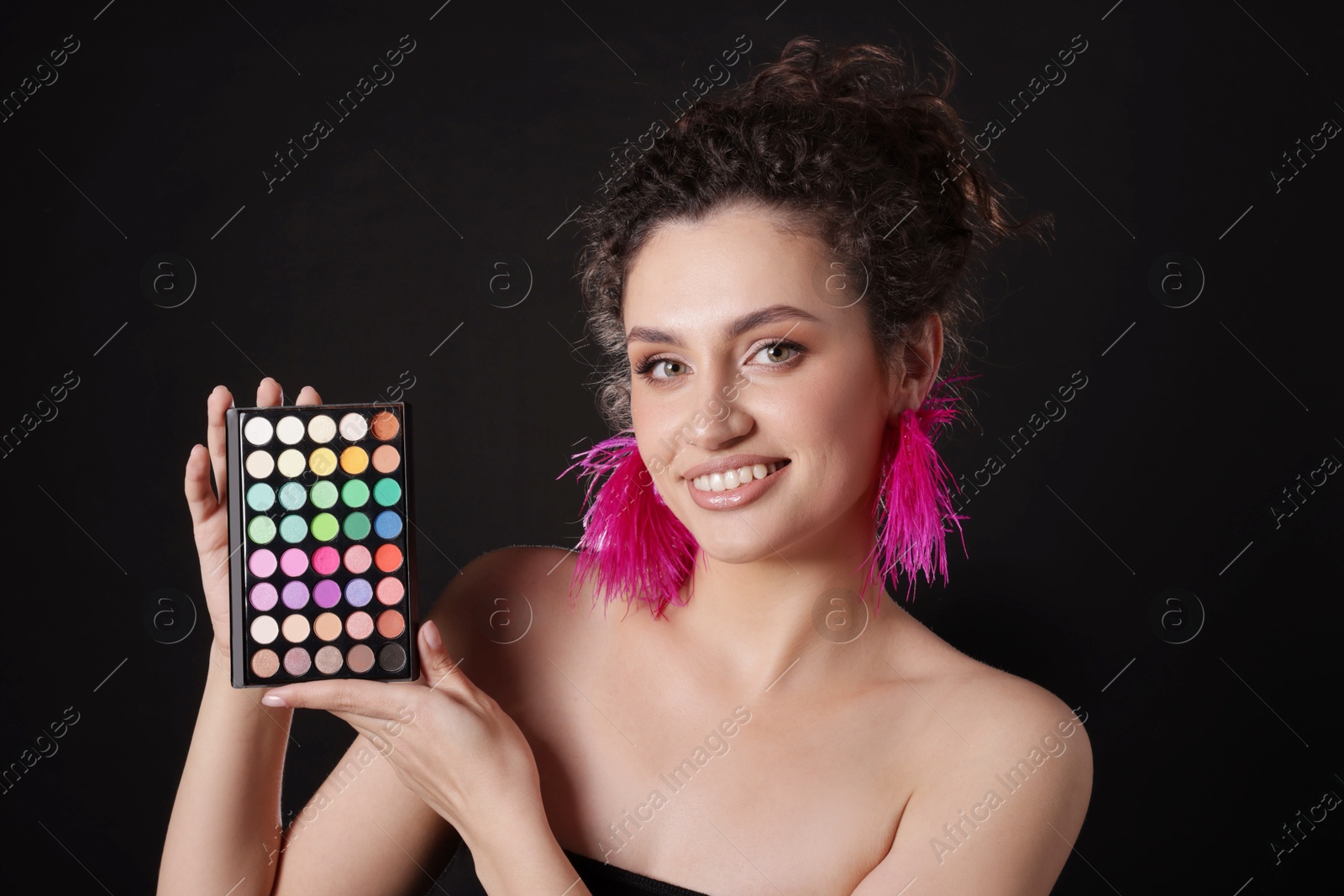 Smiling woman with bright eyeshadow palette on black background Photo of Smiling woman with bright eyeshadow palette on black background
