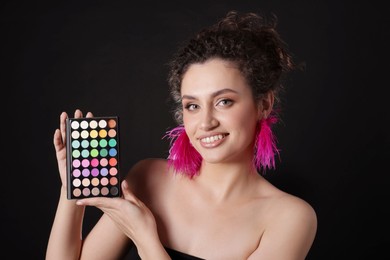 Photo of Smiling woman with bright eyeshadow palette on black background