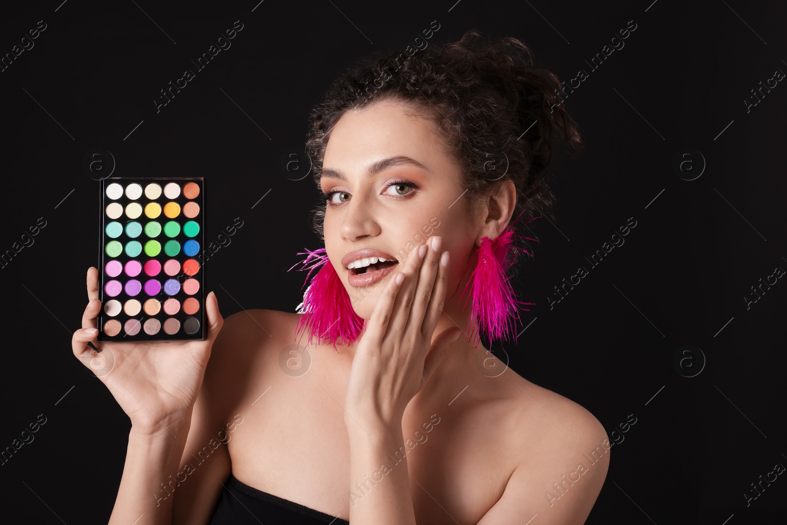 Surprised woman with bright eyeshadow palette on black background Photo of Surprised woman with bright eyeshadow palette on black background