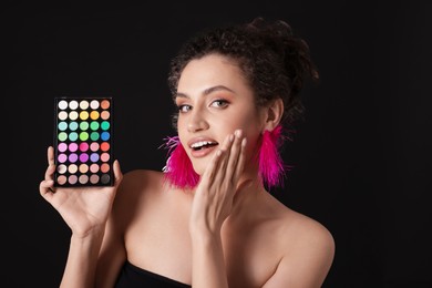 Photo of Surprised woman with bright eyeshadow palette on black background