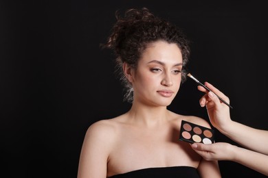 Photo of Makeup artist applying eyeshadows onto woman's face on black background, closeup. Space for text