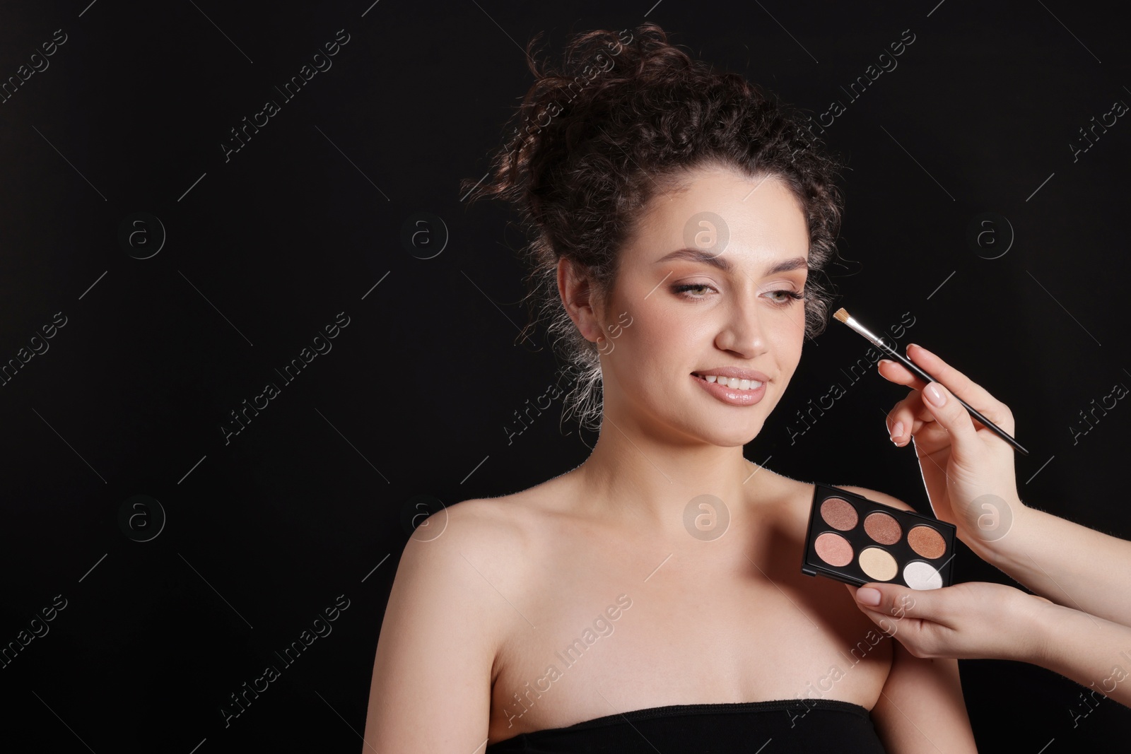 Makeup artist applying eyeshadows onto woman's face on black background, closeup. Space for text Photo of Makeup artist applying eyeshadows onto woman's face on black background, closeup. Space for text