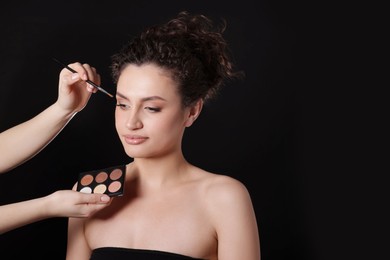 Photo of Makeup artist applying eyeshadows onto woman's face on black background, closeup