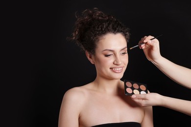 Photo of Makeup artist applying eyeshadows onto woman's face on black background, closeup