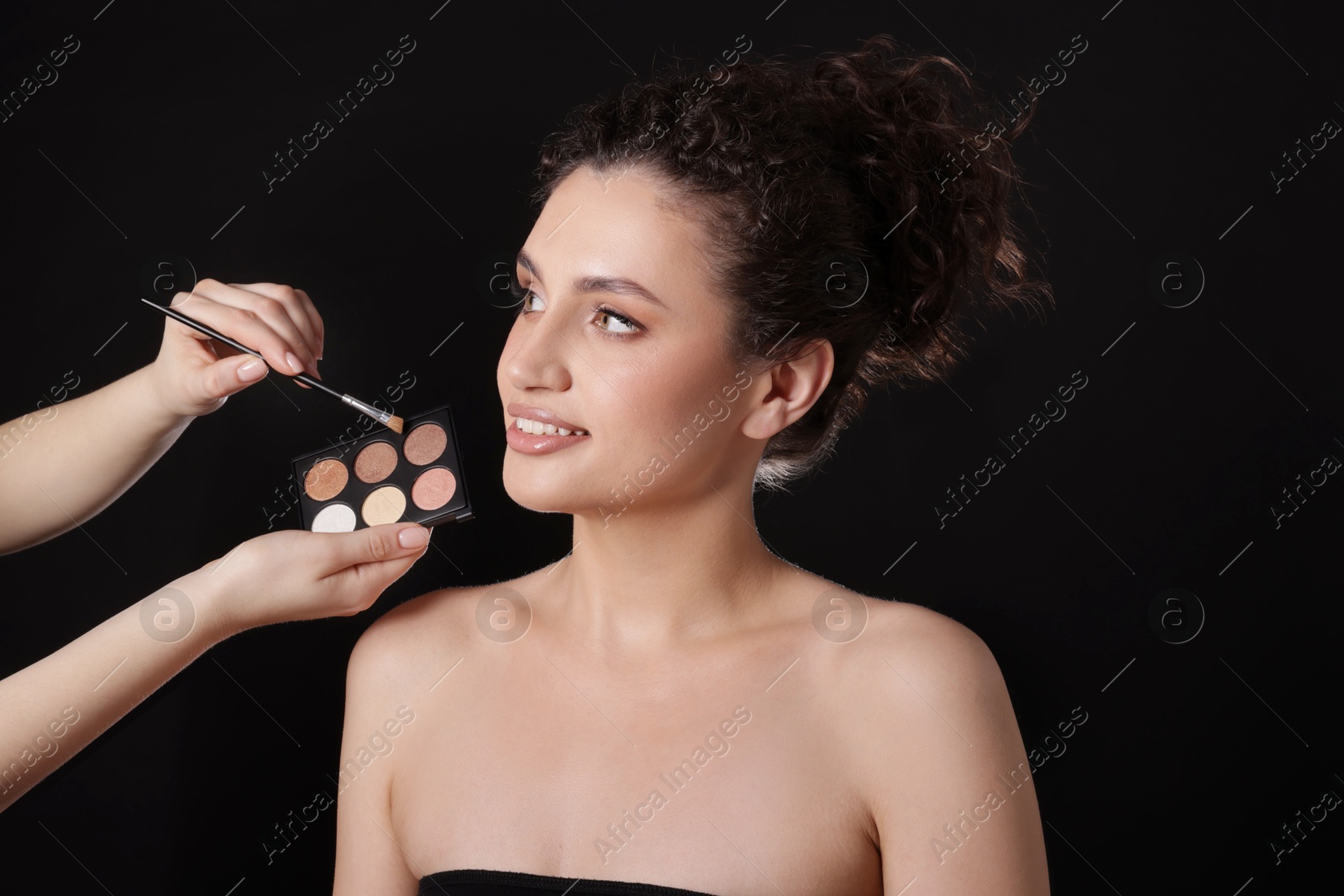 Makeup artist applying eyeshadows onto woman's face on black background, closeup Photo of Makeup artist applying eyeshadows onto woman's face on black background, closeup