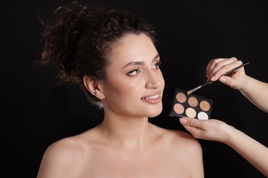 Photo of Makeup artist applying eyeshadows onto woman's face on black background, closeup