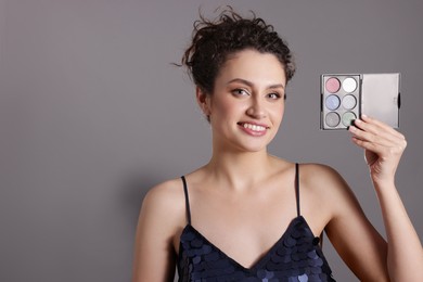 Photo of Smiling woman with eyeshadow palette on grey background. Space for text