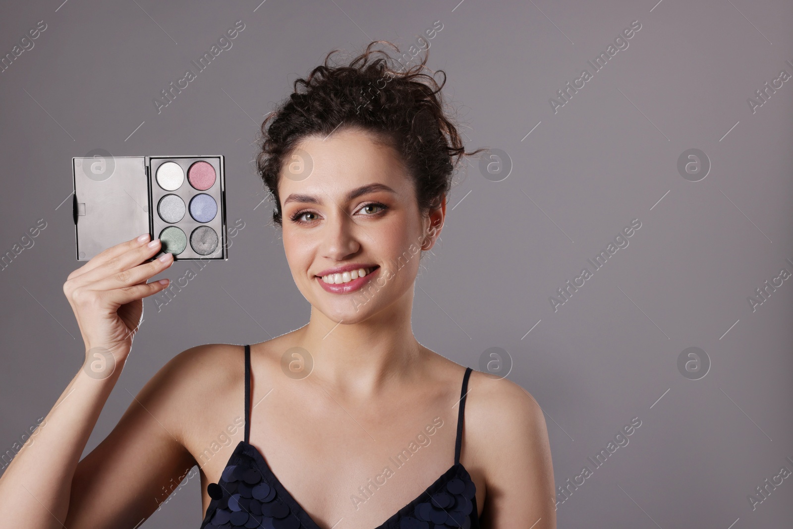 Smiling woman with eyeshadow palette on grey background. Space for text Photo of Smiling woman with eyeshadow palette on grey background. Space for text